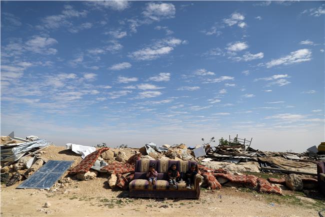 أطفال فلسطينيون يجلسون على أريكة بعد تدمير مبنى بـ«العيزرية» - صورة من رويترز