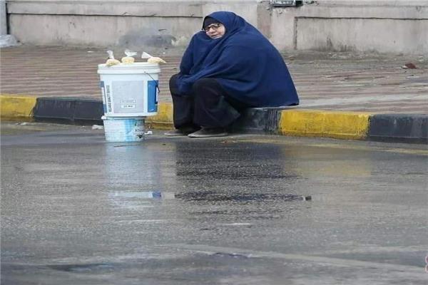 سيدة مسنه تجلس علي الرصيف في عز المطر