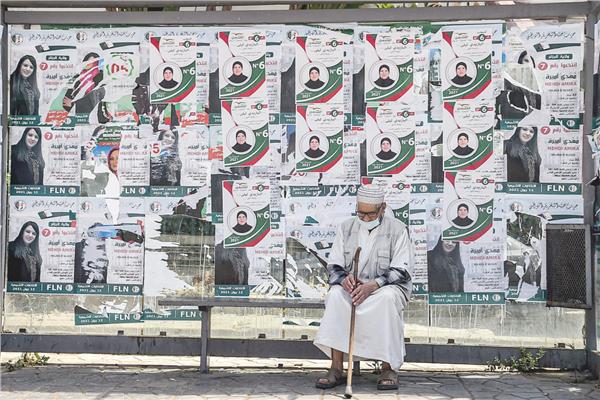 رجل مسن يجلس فى محطة حافلات مغطاة بلافتات انتخابية