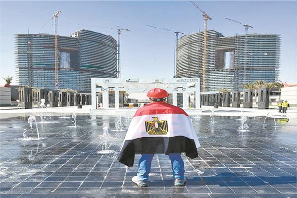 المهندس الذي يرتدي علم مصر أمام إحدى الأبراج بمدينة العلمين الجديدة