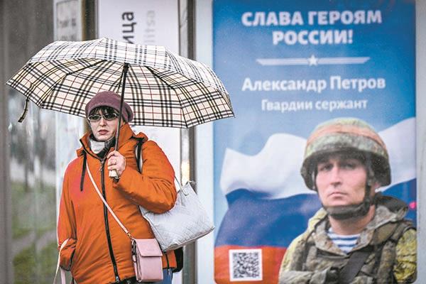 ■ أحد المشاة يمر بجوار ملصق لجندي روسي يحمل شعارًا مكتوبًا عليه  «المجد لأبطال روسيا 