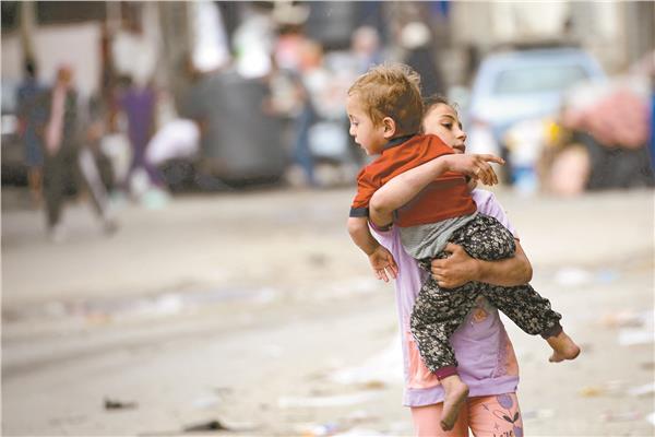 طفلة فلسطينية تحمل أخاها هربًا من رفح