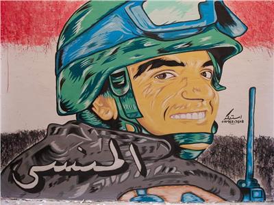 طالب بجامعة أسيوط يرسم لوحة فنية للشهيد أحمد المنسى على أحد الجدران بالقوصية