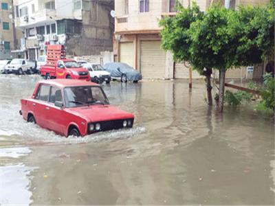 < المياه تغرق الشوارع وفى الإطار جانب من أعمال إزالة آثار الأمطار