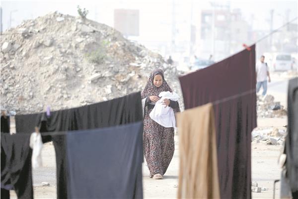 امرأة فلسطينية تحمل طفلًا أثناء سيرها قرب مخيم النصيرات للاجئين فى وسط قطاع غزة    